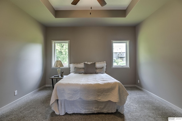 carpeted bedroom featuring a tray ceiling and ceiling fan