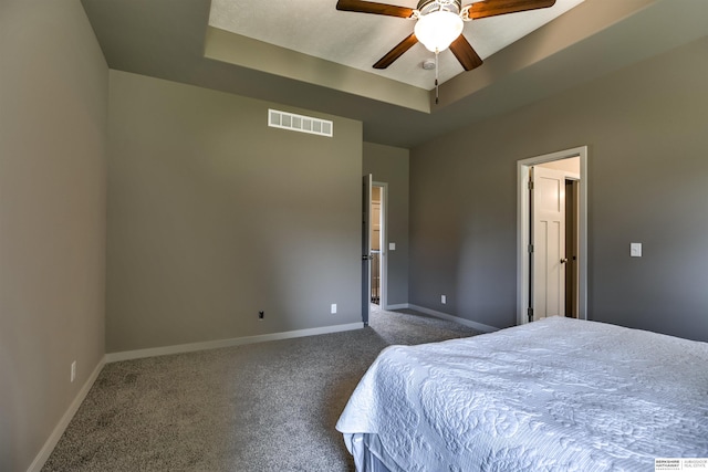 bedroom with ceiling fan, dark carpet, and a raised ceiling