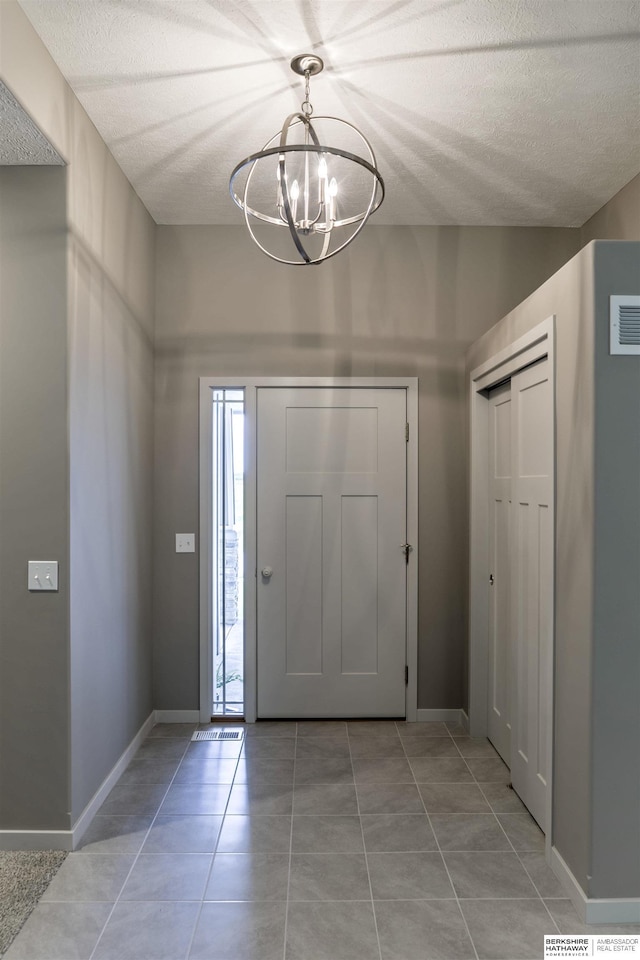 tiled entrance foyer featuring a notable chandelier and a textured ceiling