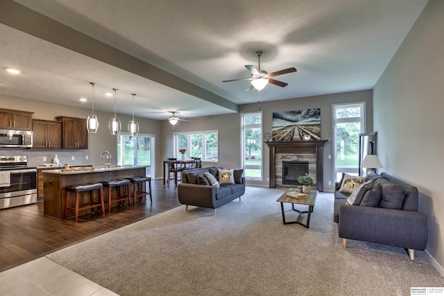 living room with dark hardwood / wood-style flooring, a stone fireplace, a wealth of natural light, and ceiling fan