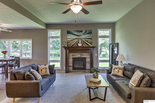 living room with a textured ceiling, ceiling fan, a fireplace, and light carpet