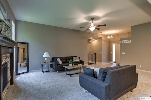 carpeted living room featuring a stone fireplace and ceiling fan with notable chandelier