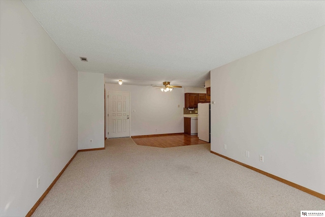 unfurnished living room featuring light carpet, ceiling fan, and a textured ceiling