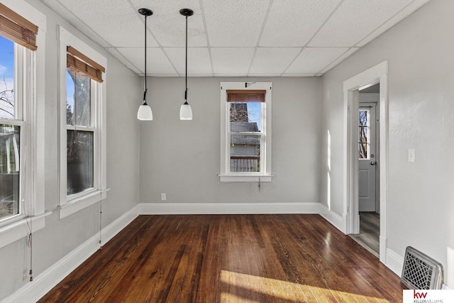 unfurnished dining area with a paneled ceiling and dark wood-type flooring