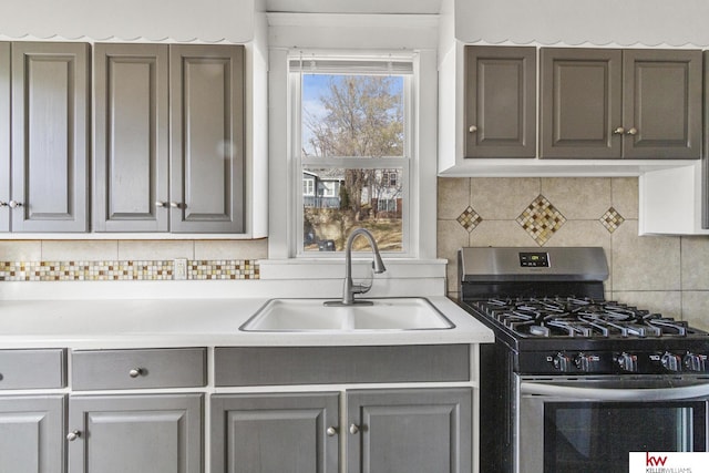 kitchen with decorative backsplash, gray cabinets, stainless steel range with gas cooktop, and sink