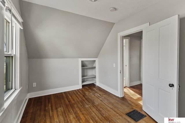 additional living space featuring a textured ceiling, dark hardwood / wood-style flooring, and lofted ceiling