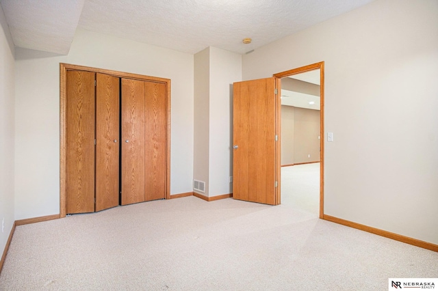 unfurnished bedroom with a textured ceiling, light carpet, and a closet