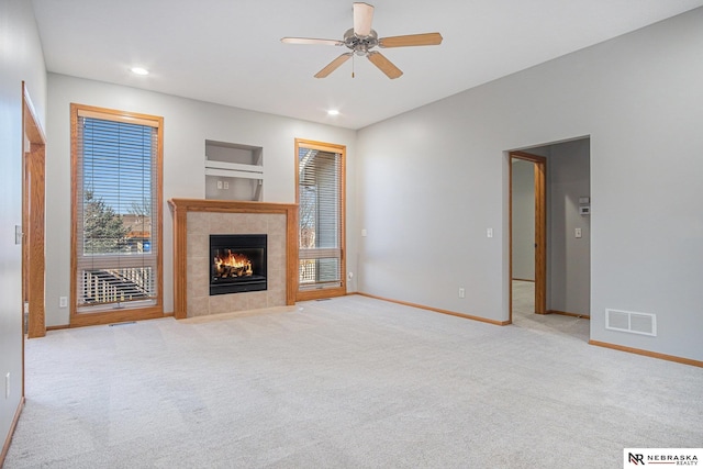 unfurnished living room with a tiled fireplace, ceiling fan, and light colored carpet