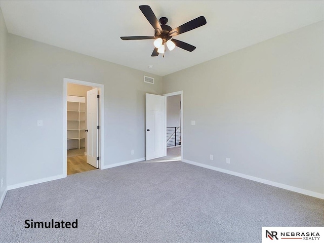 unfurnished bedroom featuring a spacious closet, a closet, ceiling fan, and light carpet