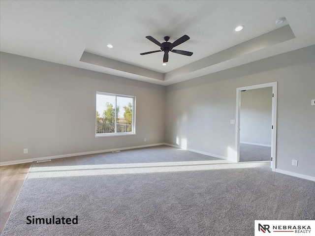 unfurnished room with a raised ceiling, ceiling fan, and light wood-type flooring