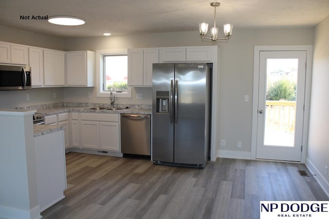 kitchen featuring white cabinetry, sink, hanging light fixtures, appliances with stainless steel finishes, and hardwood / wood-style flooring