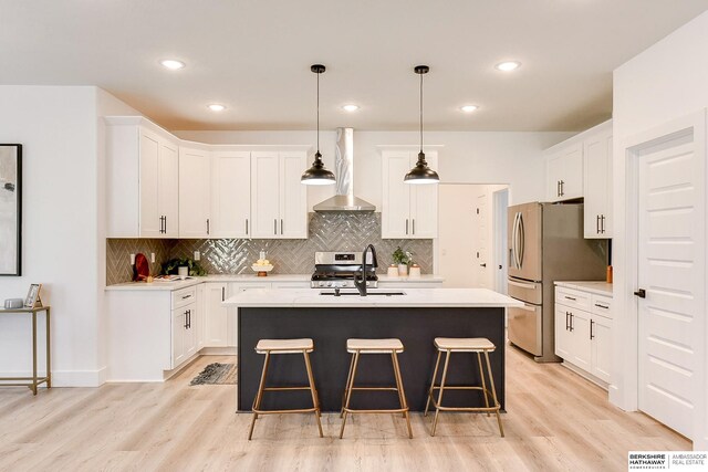 kitchen featuring white cabinetry, a kitchen island with sink, wall chimney range hood, and light wood-type flooring