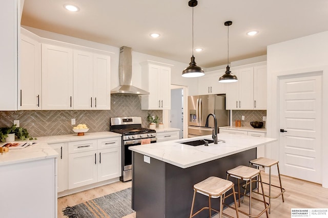 kitchen with white cabinets, stainless steel appliances, a center island with sink, and wall chimney exhaust hood