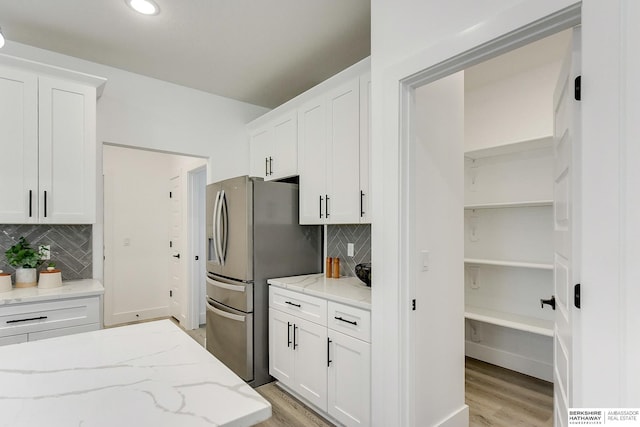 kitchen with light wood-type flooring, tasteful backsplash, light stone counters, stainless steel fridge with ice dispenser, and white cabinetry