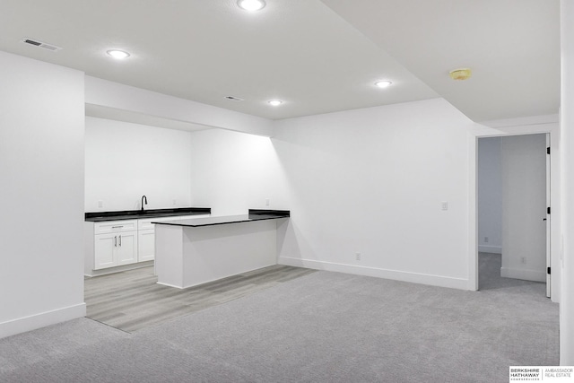 kitchen with kitchen peninsula, sink, white cabinets, and light colored carpet