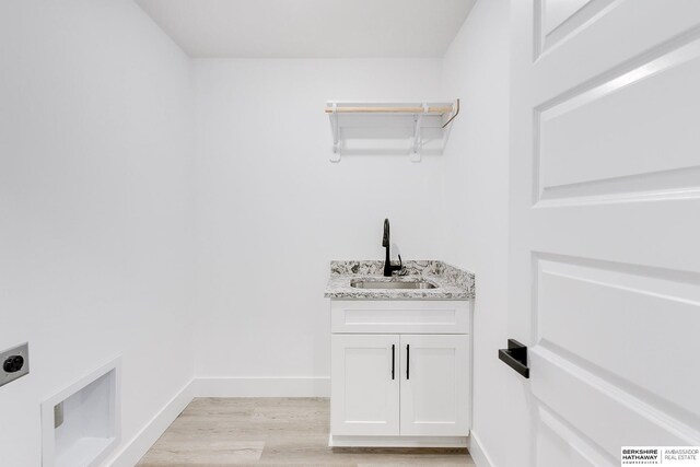 washroom featuring electric dryer hookup, sink, cabinets, and light wood-type flooring