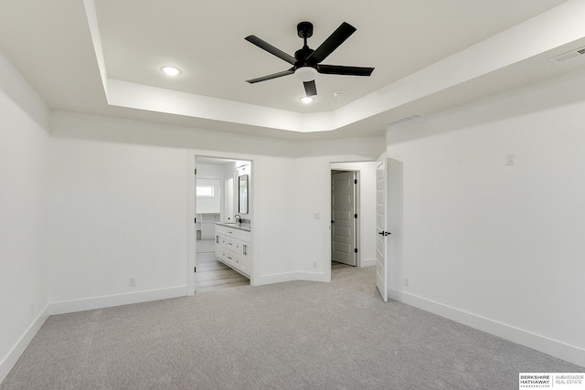 unfurnished bedroom with ensuite bathroom, a raised ceiling, ceiling fan, and light colored carpet