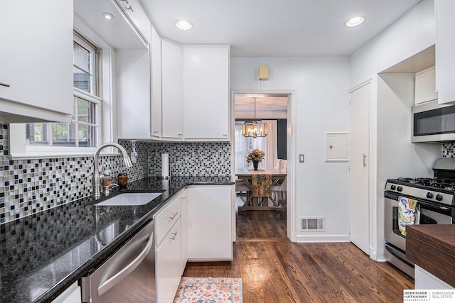 kitchen with sink, stainless steel appliances, dark stone counters, decorative light fixtures, and white cabinets