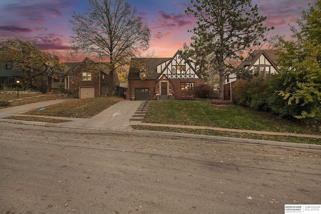 tudor-style house featuring a garage and a lawn