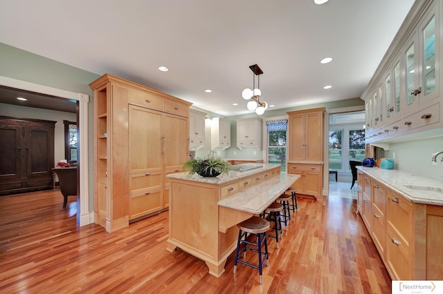 kitchen with light wood-type flooring, light brown cabinetry, a center island, and sink