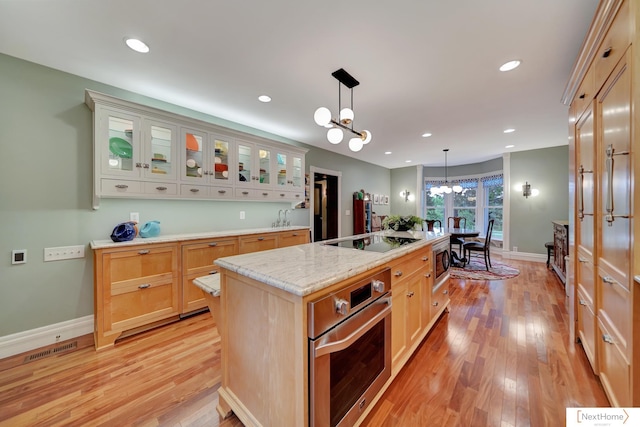 kitchen with light brown cabinets, a kitchen island with sink, an inviting chandelier, light hardwood / wood-style flooring, and appliances with stainless steel finishes