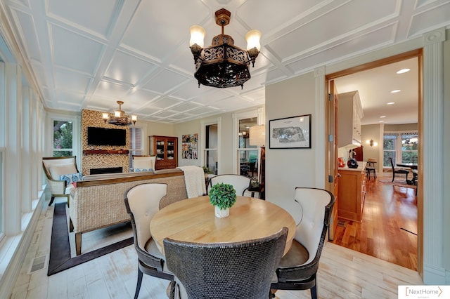 dining space with a large fireplace, an inviting chandelier, coffered ceiling, and light wood-type flooring