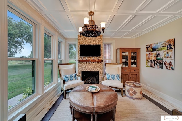 living area featuring a fireplace, a healthy amount of sunlight, coffered ceiling, and a notable chandelier