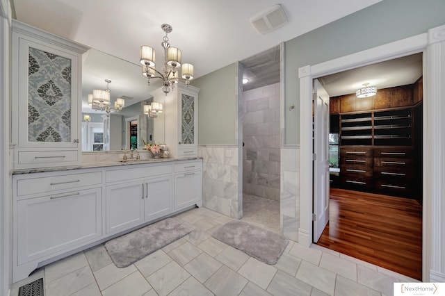 bathroom with vanity, an inviting chandelier, tile walls, walk in shower, and wood-type flooring