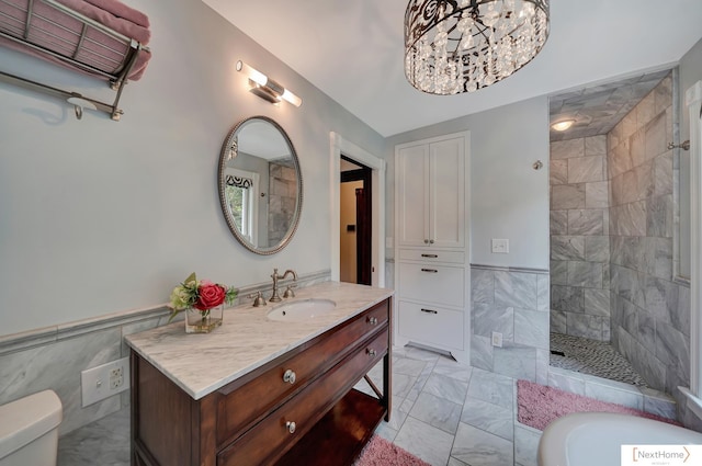 bathroom with a tile shower, a chandelier, toilet, vanity, and tile walls