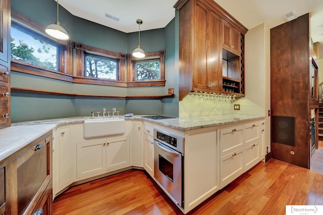 kitchen with sink, oven, decorative light fixtures, and light wood-type flooring