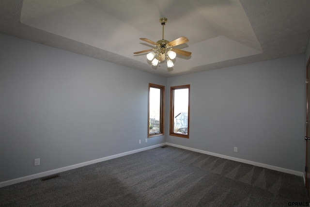 unfurnished room with a raised ceiling, ceiling fan, and dark carpet