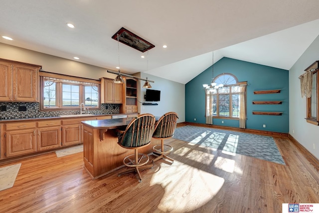 kitchen with a kitchen bar, backsplash, decorative light fixtures, light hardwood / wood-style floors, and a kitchen island