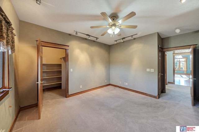 unfurnished bedroom featuring a walk in closet, ceiling fan, light carpet, and track lighting