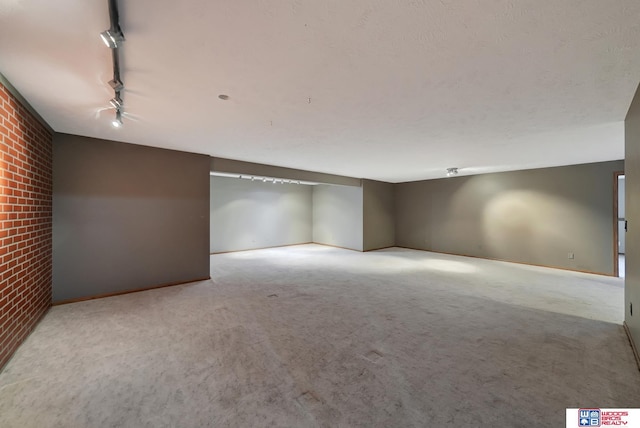 empty room featuring rail lighting, light colored carpet, and brick wall