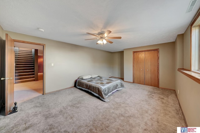 bedroom with ceiling fan, a closet, light colored carpet, and a textured ceiling