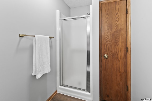 bathroom with a textured ceiling, hardwood / wood-style flooring, and a shower with door