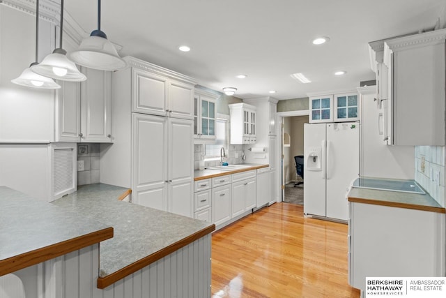 kitchen featuring white cabinetry, sink, white refrigerator with ice dispenser, pendant lighting, and light hardwood / wood-style floors