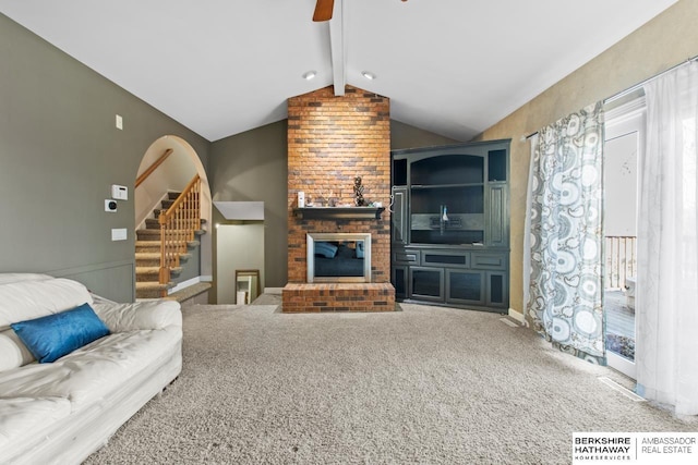 carpeted living room with ceiling fan, lofted ceiling with beams, a wealth of natural light, and a brick fireplace