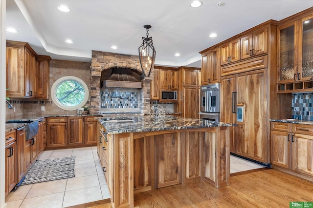 kitchen featuring hanging light fixtures, light hardwood / wood-style flooring, built in appliances, dark stone countertops, and a kitchen island