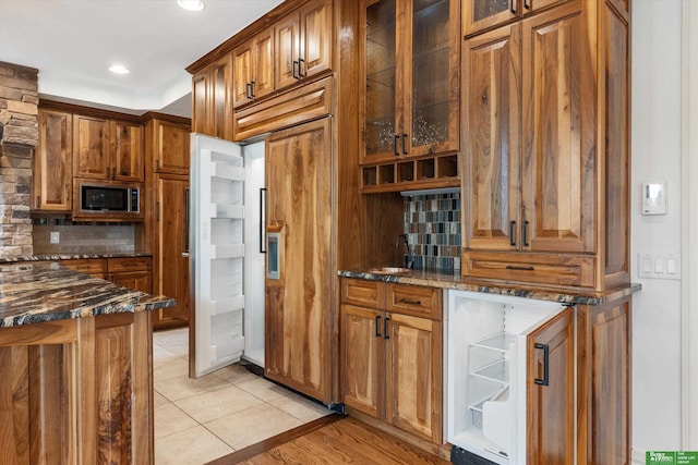 kitchen with built in appliances, light hardwood / wood-style flooring, dark stone counters, and tasteful backsplash