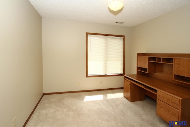 unfurnished office with built in desk, light colored carpet, and a textured ceiling