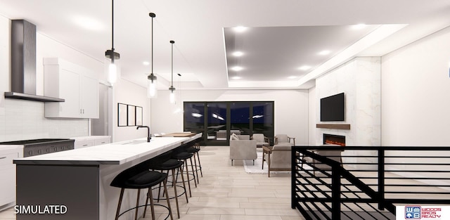 kitchen featuring a premium fireplace, an island with sink, white cabinetry, and wall chimney range hood