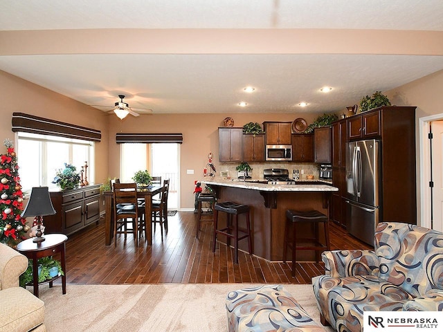 kitchen with a kitchen island, a breakfast bar area, appliances with stainless steel finishes, ceiling fan, and dark brown cabinets