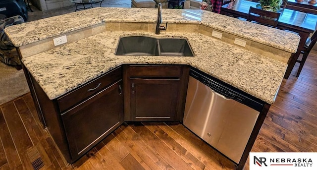 kitchen with light stone countertops, dark wood-type flooring, sink, dark brown cabinets, and stainless steel dishwasher