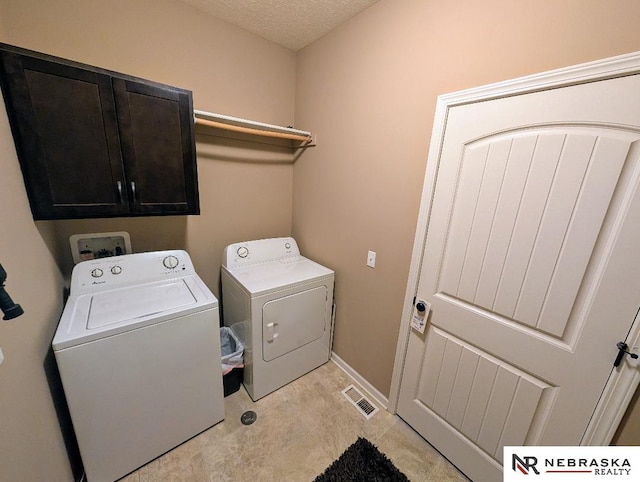 clothes washing area with a textured ceiling, separate washer and dryer, and cabinets