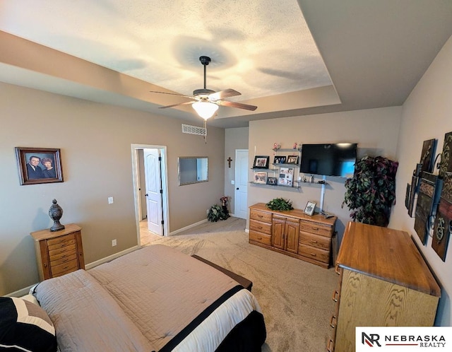 bedroom with a textured ceiling, light carpet, ceiling fan, and a tray ceiling