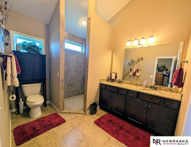 bathroom with a textured ceiling, tiled shower, vanity, and toilet