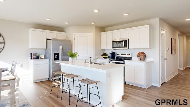 kitchen with white cabinetry, sink, stainless steel appliances, and a center island with sink