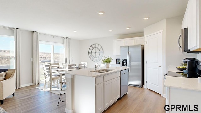 kitchen featuring appliances with stainless steel finishes, sink, light hardwood / wood-style flooring, white cabinetry, and an island with sink