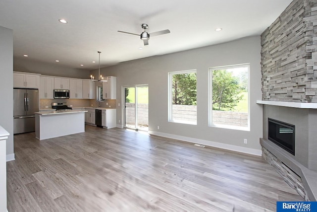 kitchen with pendant lighting, a stone fireplace, light wood-type flooring, appliances with stainless steel finishes, and white cabinetry